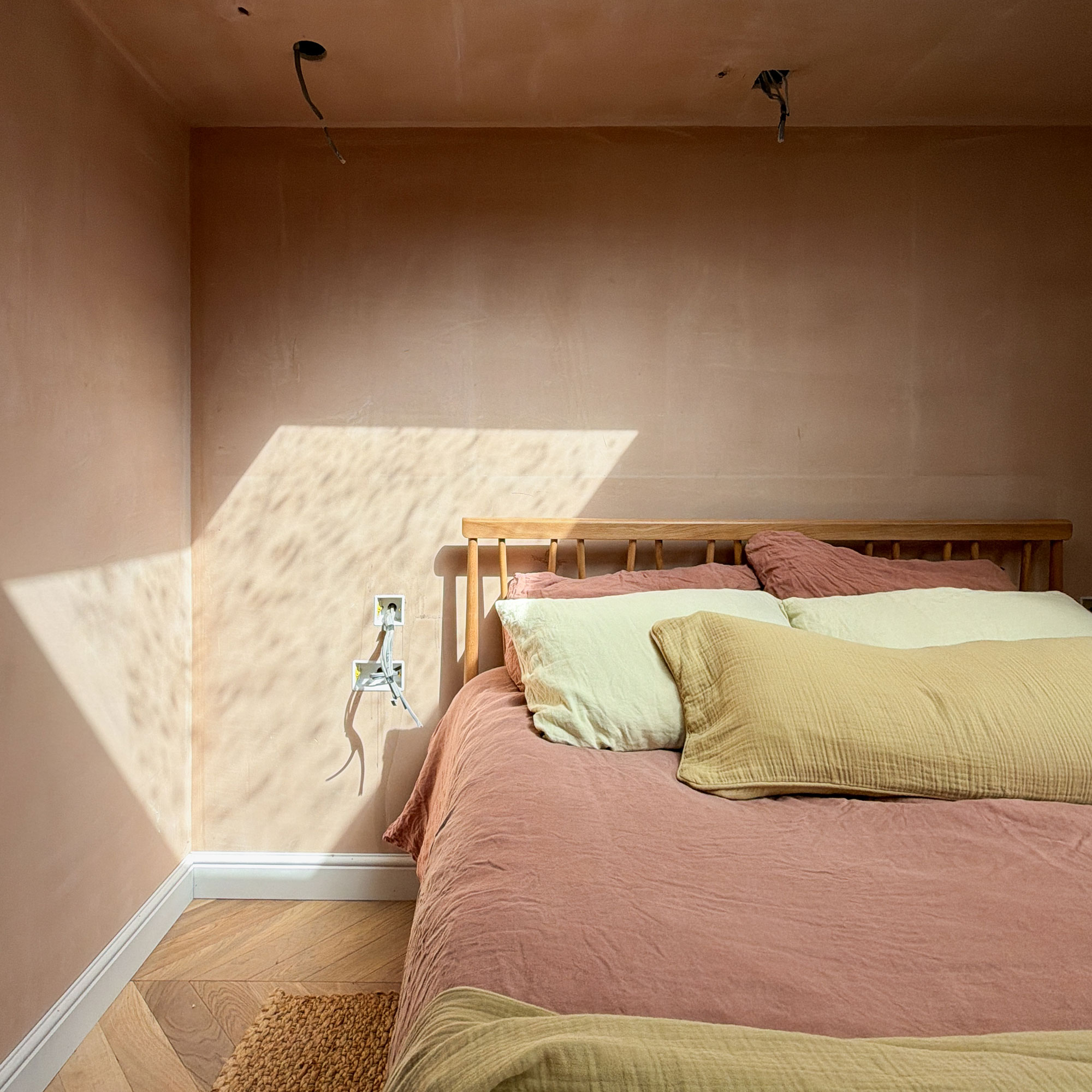 Peach bedroom with exposed wiring and bed covered with pink and yellow linens