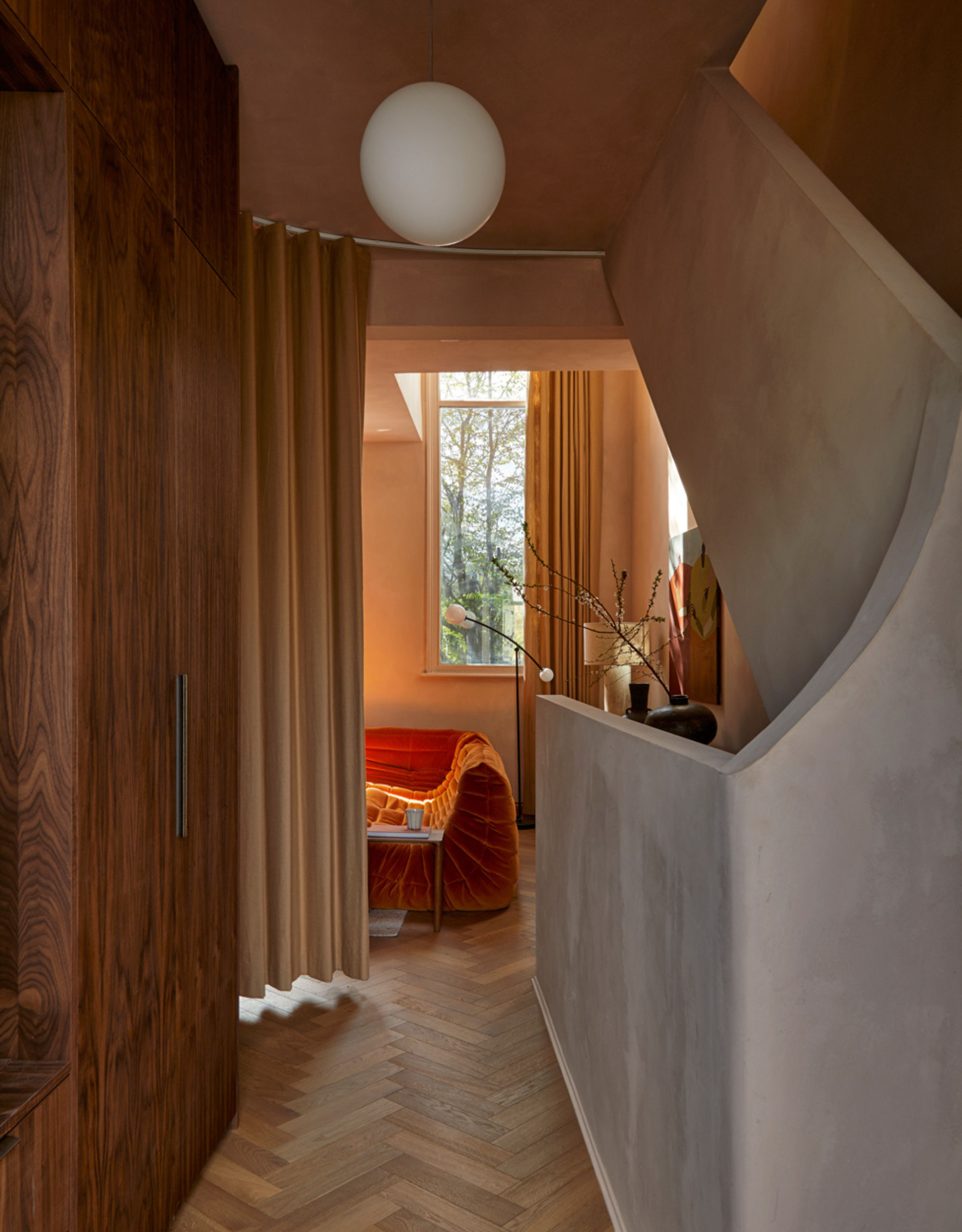 A minimalist hallway with dark wood cupboards by a staircase, an orange Togo, and a spherical pendant lamp