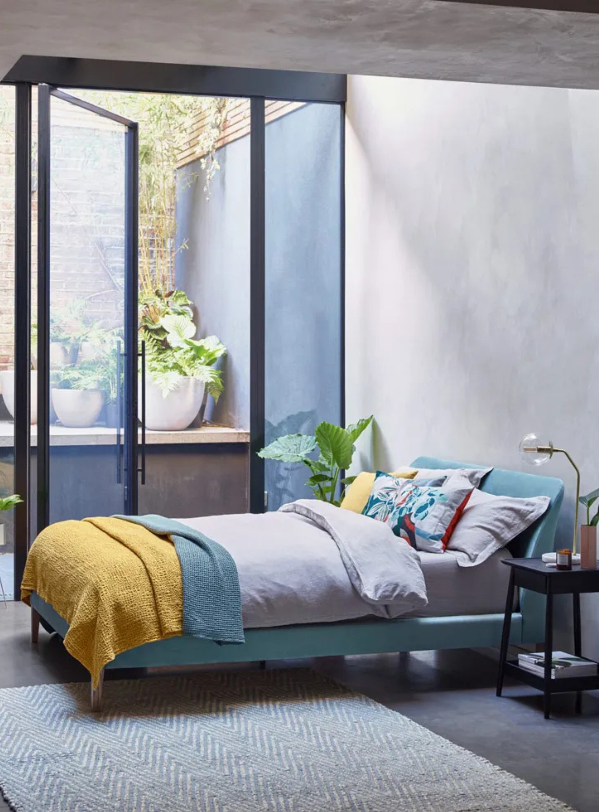 blue bed in a gray bedroom with windows out to an internal courtyard