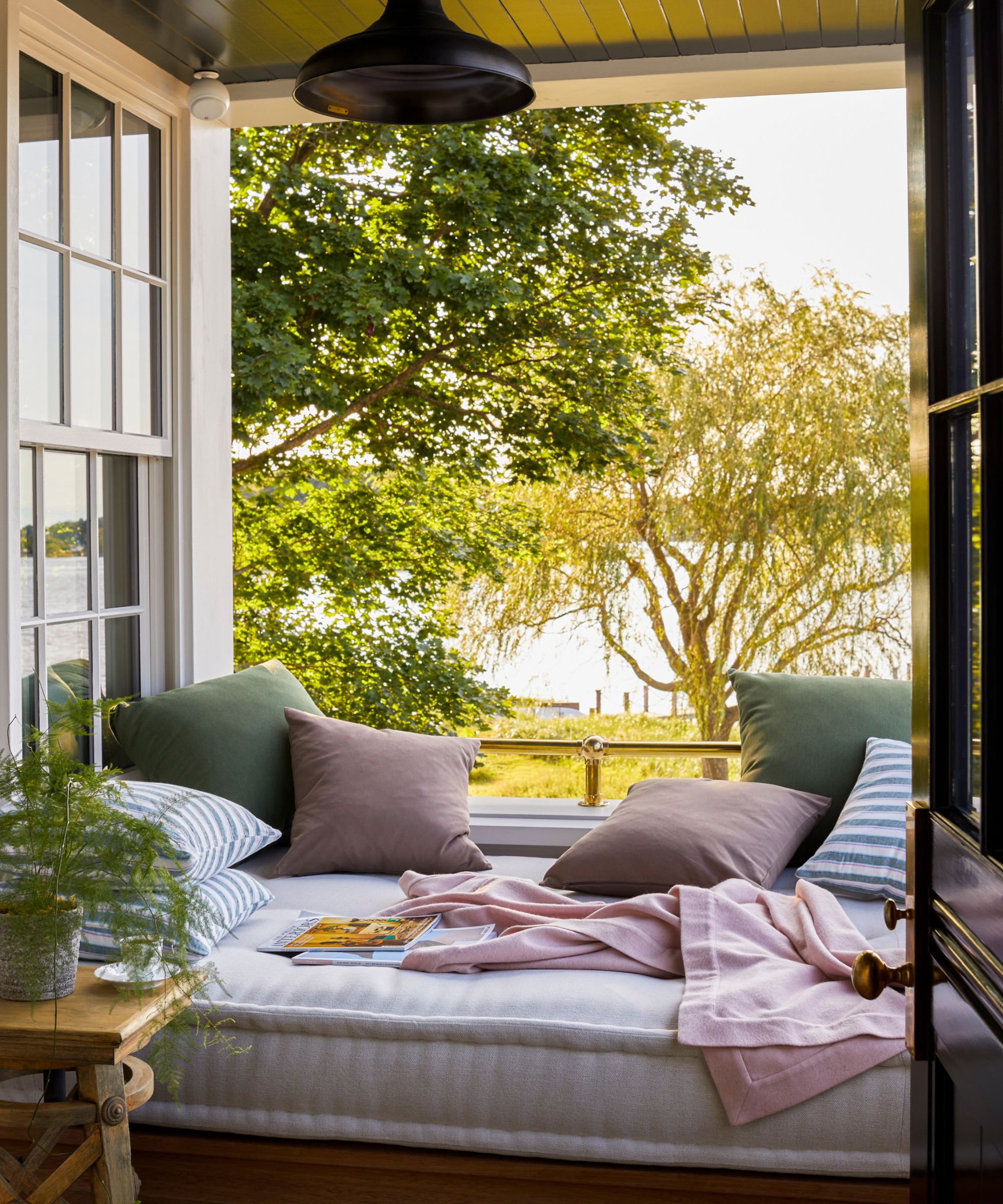 Sleeping porch with open window with summery bedding and cushions, side table with plant