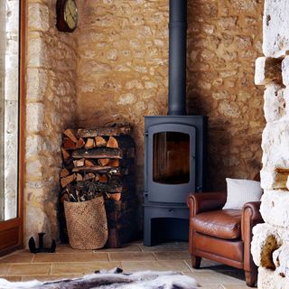 exposed stone wall and wood burner and wood stacks and armchair