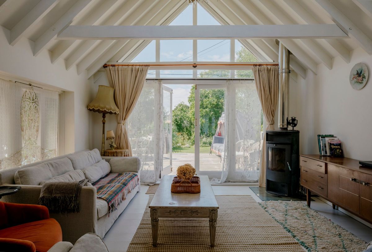 The living room with log burner leads onto the outside decking through white bifold doors and curtains