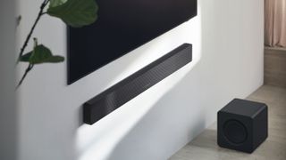 Samsung HW-Q700F soundbar mounted on a wall with a plant in the foreground and subwoofer on the floor