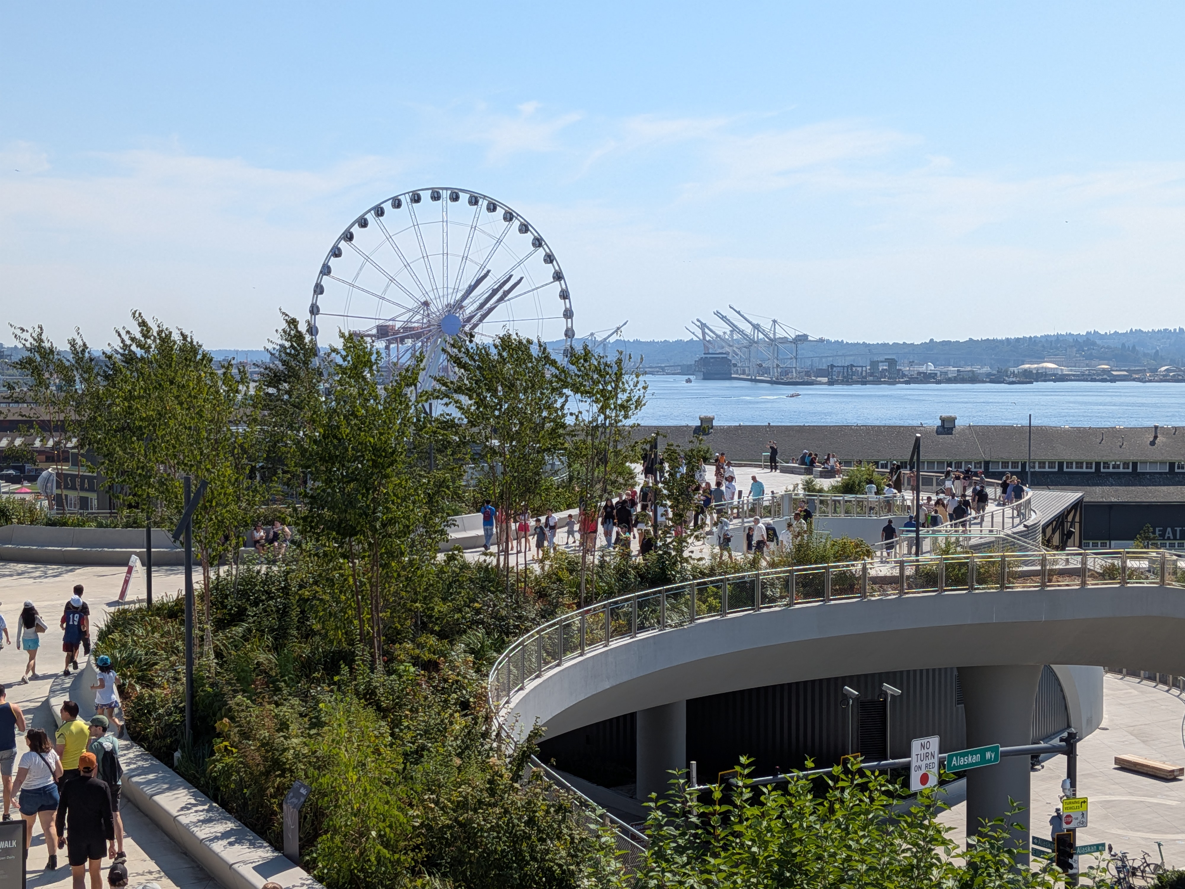 A raised walkway with greenery, people, and a Ferris Wheel in the background
