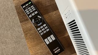 Sony remote control for Bravia Projector 8, placed on a wooden coffee table next to projector device