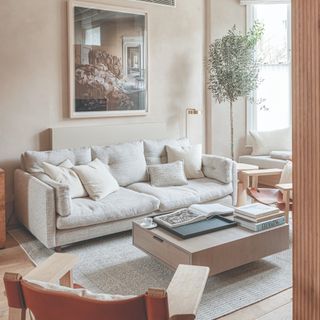 A living room with a low deep light beige sofa and beige limewash walls with a storage coffee table in the centre of the room