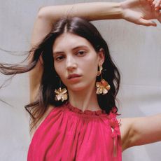 Young brunette woman looking at camera, wearing Fabrique pink dress and big gold flower earrings.