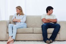 A couple sits on a couch looking away from each other.
