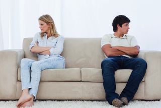 A couple sits on a couch looking away from each other.