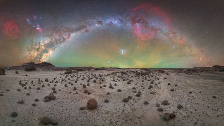 Desert landscape scattered with round stones under a vivid Milky Way arch and colorful night sky