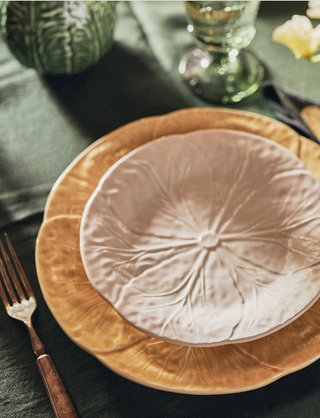 a white cabbage plate stacked on top of a larger yellow cabbage plate on a set table