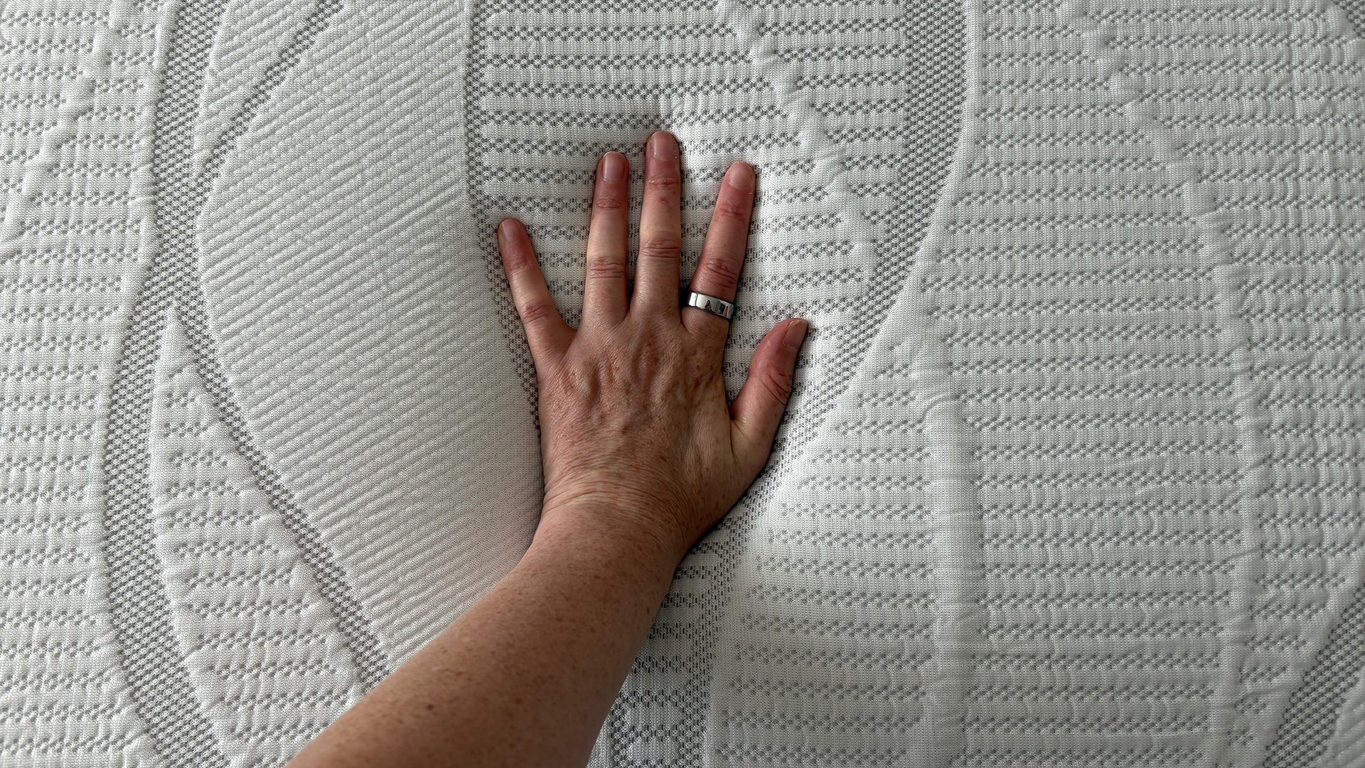 A close up of a hand pressing into the surface of the DreamCloud Softer Mattress Topper