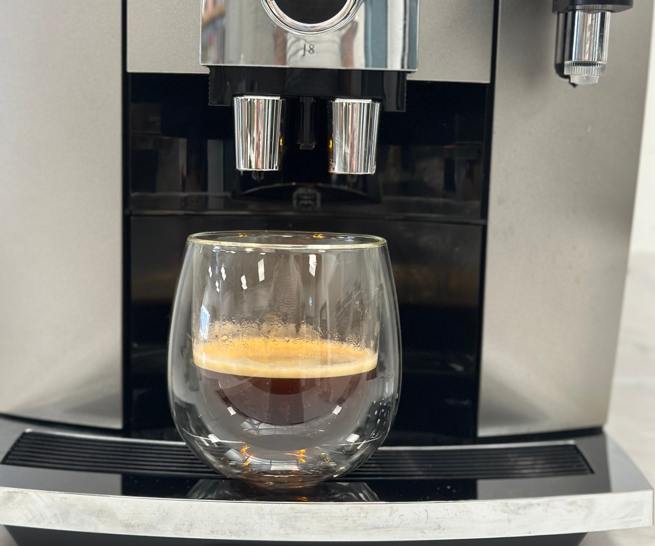 A double walled glass espresso glass under the spouts of an espresso machine with a single shot espresso inside.
