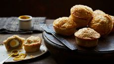 Mini lamb and egg pies on a wooden board and one at the front cut open with a spoon of mustard next to it