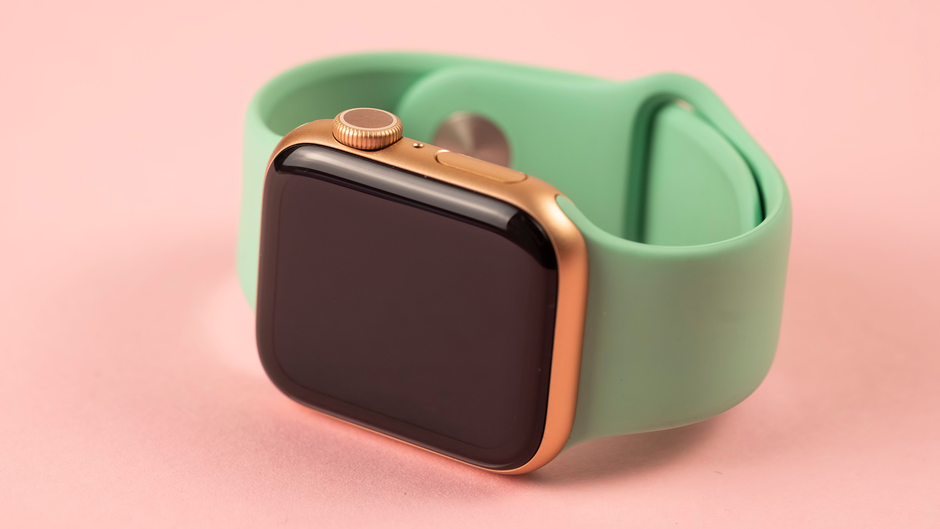 An Apple Watch with a green silicone sport band attached on a pink background