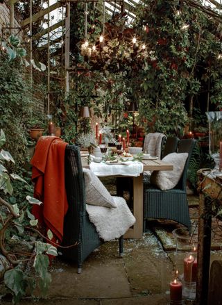 A cozy outdoor dining area with red blankets, beige cushions and candles