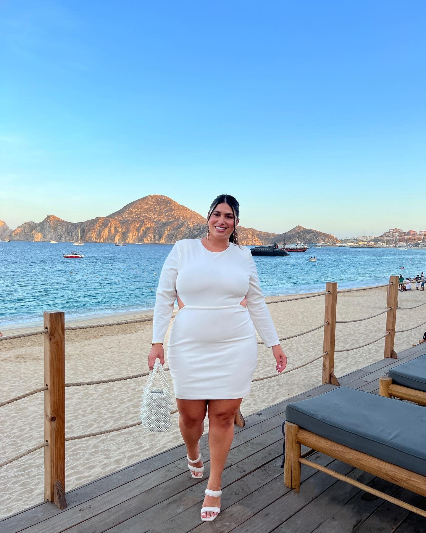 Plus size bride wearing white mini dress while on beach.