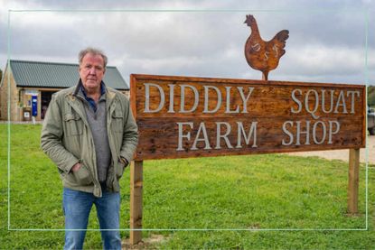 a close up of Jeremy Clarkson standing next to the Diddly Squat Farm Shop sign