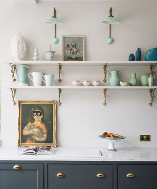 Kitchen storage ideas showing a white kitchen with open shelving on the wall and dark green drawers below