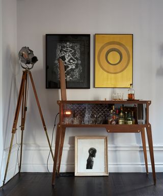 Rock star style bar cabinet with industrial tripod floor light, and cool framed prints on wall.