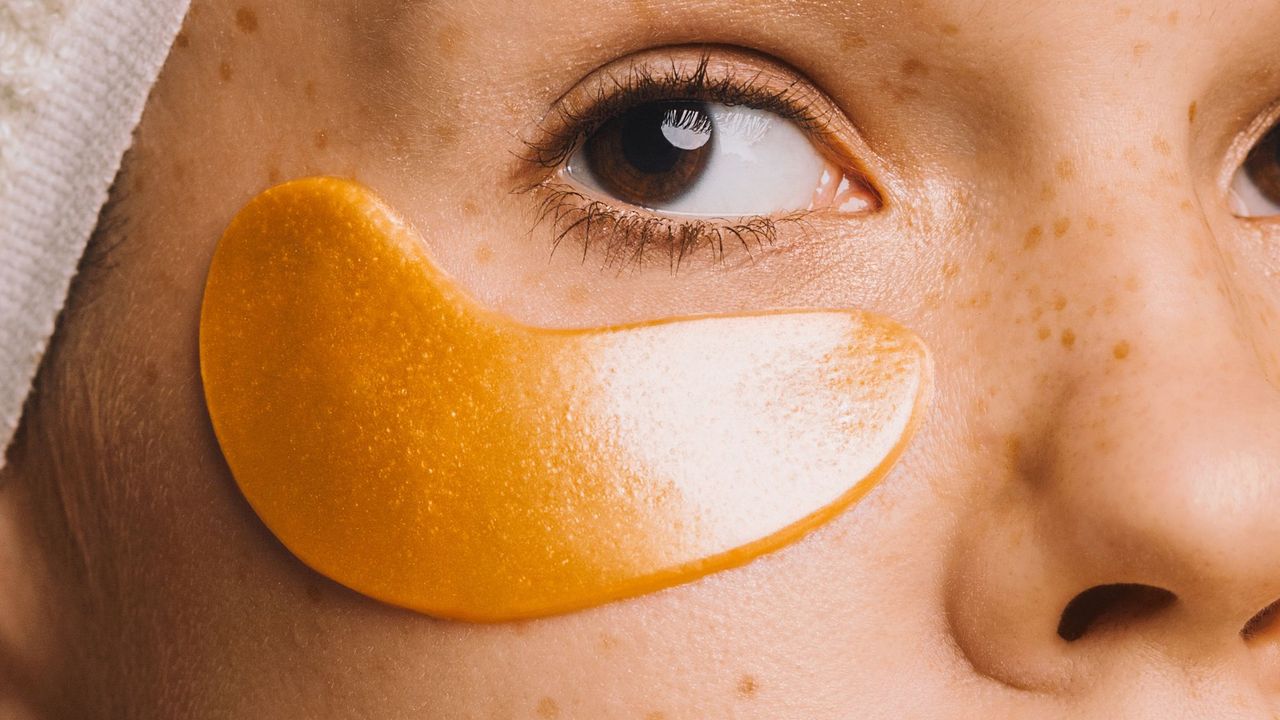 Girl in towel with gold-colored hyaluronic eye mask on her face to treat dark circles