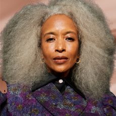 A woman with a grey afro wearing a purple floral print top