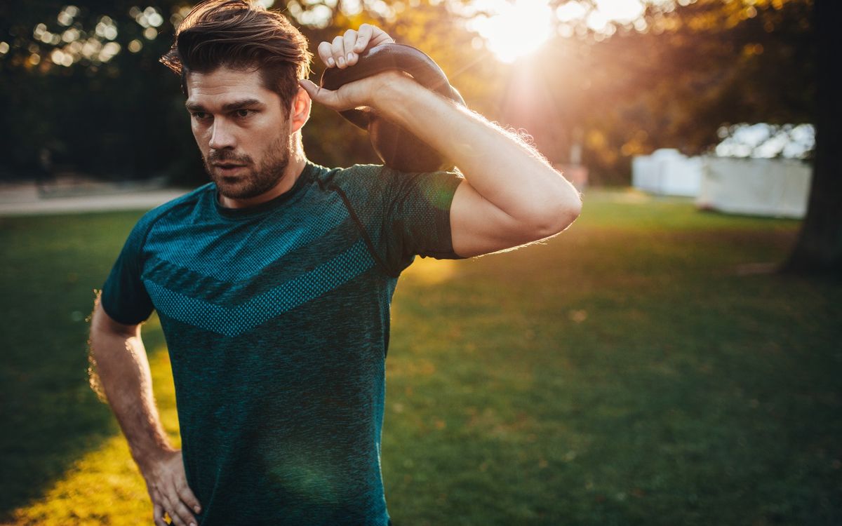 Man holding a kettlebell at his shoulder outside during workout