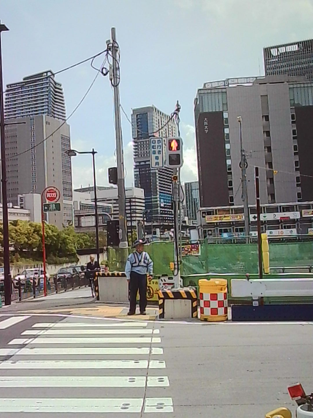 Low-resolution photo of a city crosswalk in Japan with a traffic officer and tall buildings.
