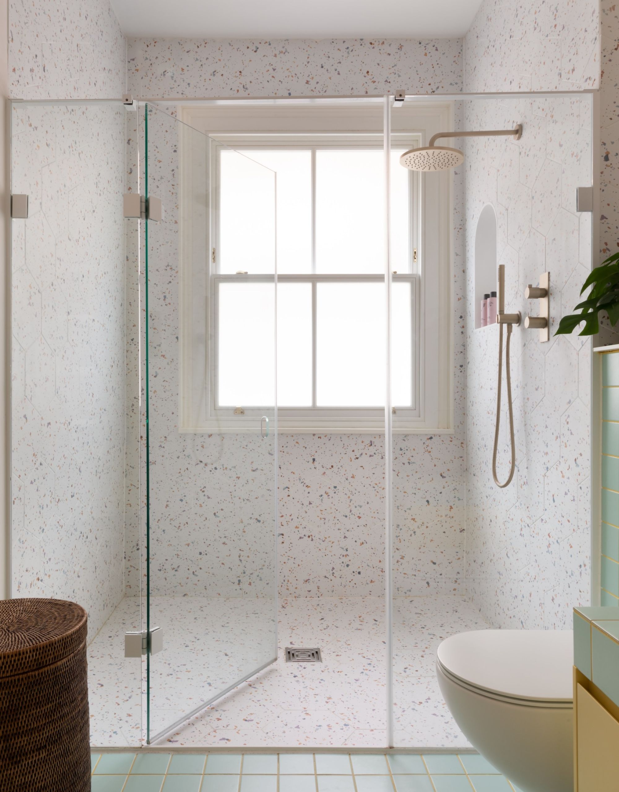 A wide wall to wall shower with speckled terrazzo tiles and frameless glass shower panels