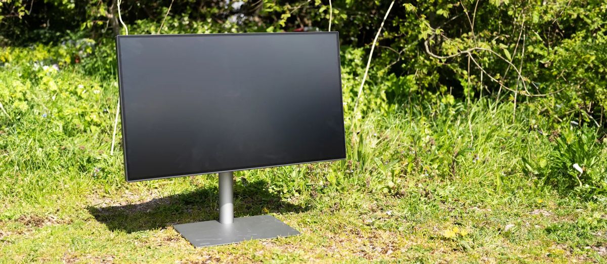 A black BenQ PD3225U monitor sitting on grass in sunshine