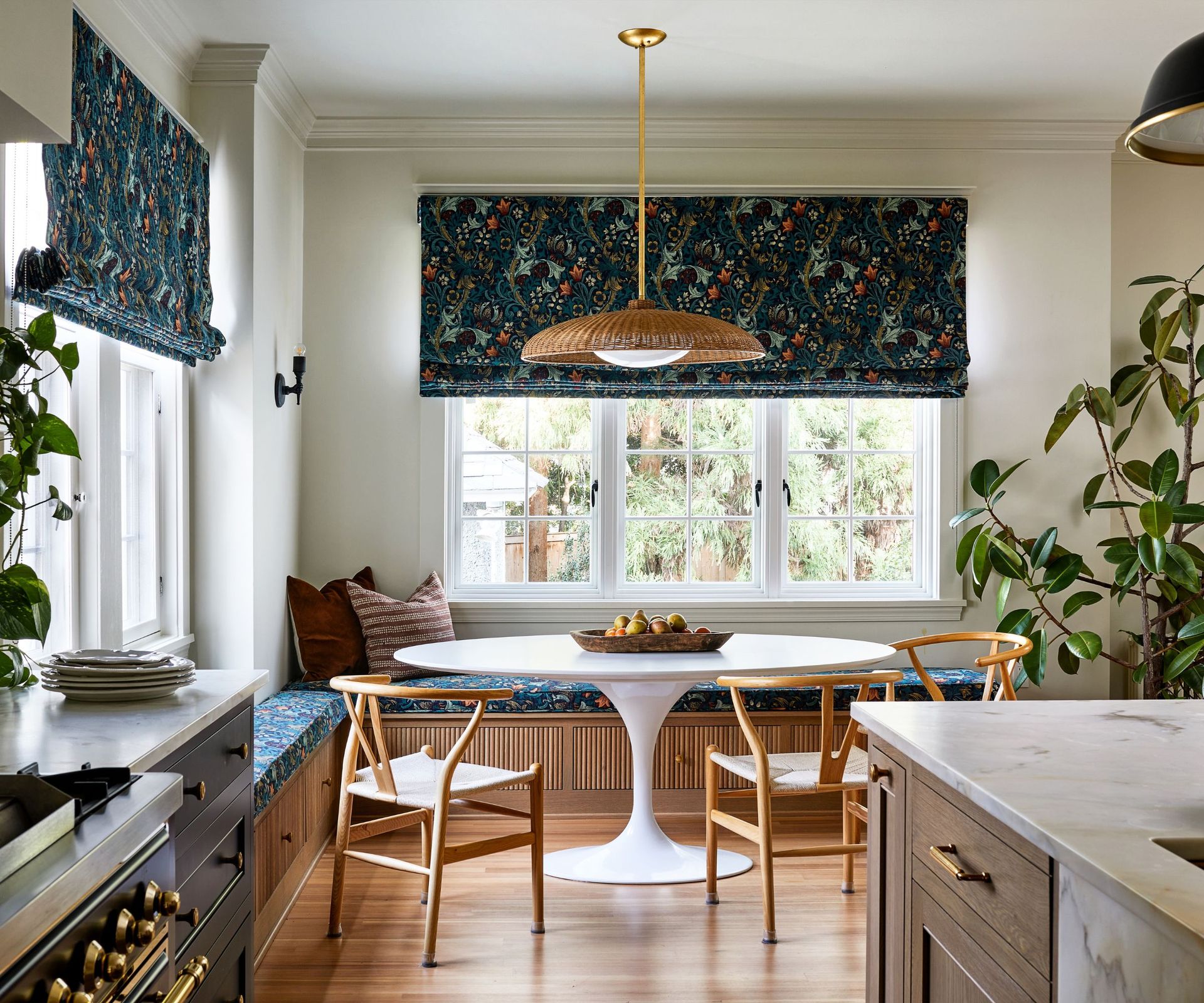 A dining nook with banquette seating and wishbone chairs around a round white table