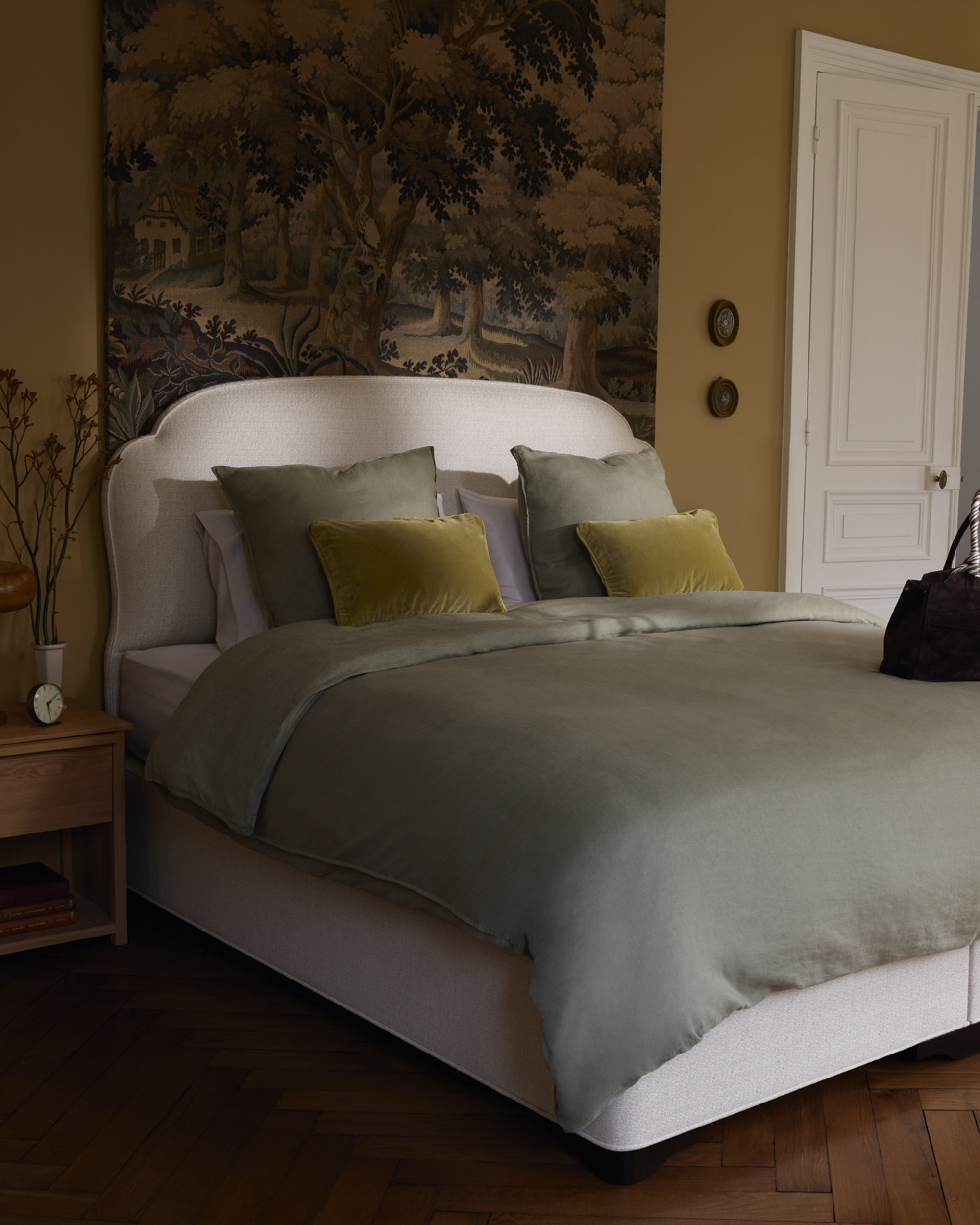 A modern bedroom with a tapestry on the wall, and a double bed with sage green bedding