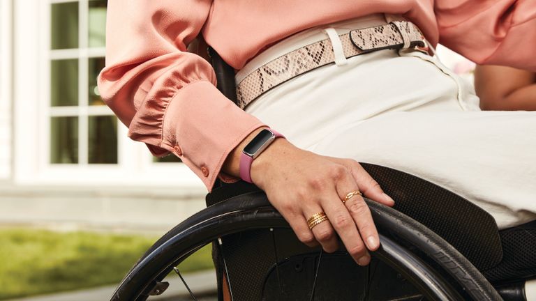 best fitness tracker: woman in wheelchair wearing a pink blouse and cream trousers, with Fitbit Luxe on her wrist