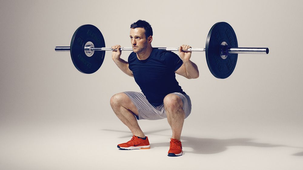 Man demonstrates the midpoint position of the barbell back squat exercise