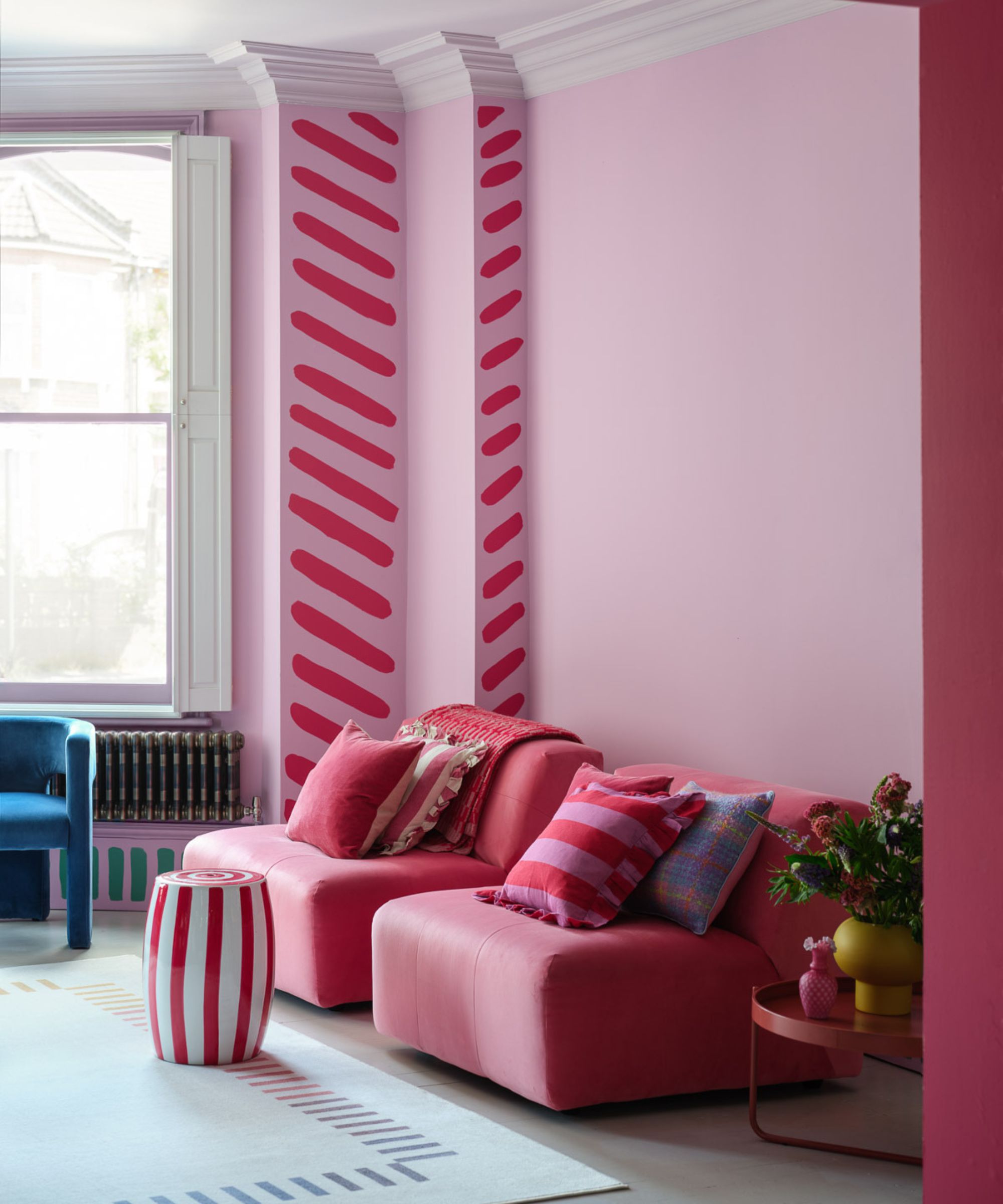 Pink painted living room walls with dark pink stripe accent. There are stripes on the rugs, foot stools, cushions and under the radiator too