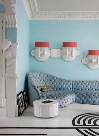 Pale blue living room with blue corner couch and orange wall lights