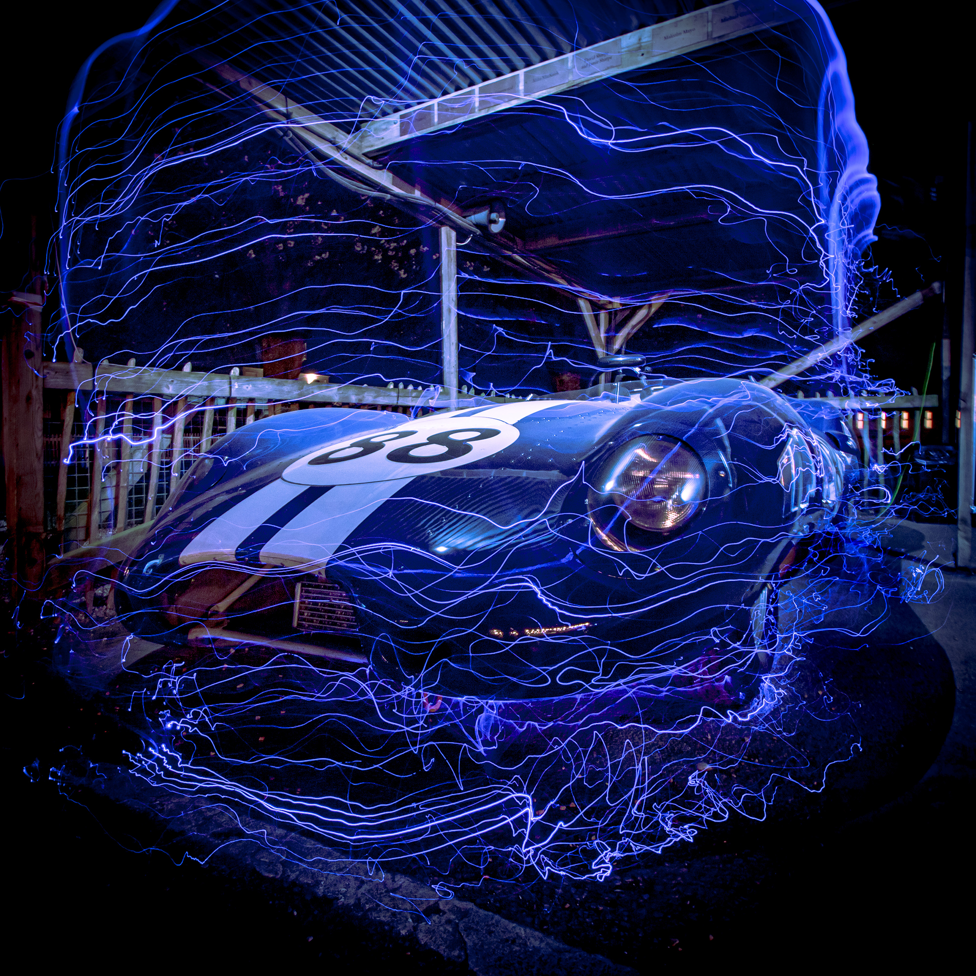A sleek blue race car with the number 38, surrounded by swirling blue light streaks, in an illuminated nighttime setting.