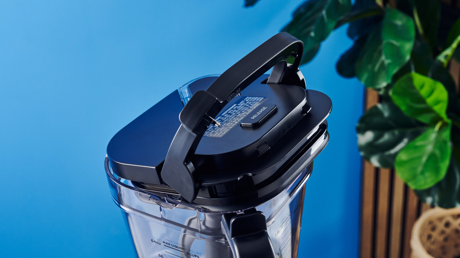 Ninja Crush Boss Blender in black photographed in front of a ble background with fruit.