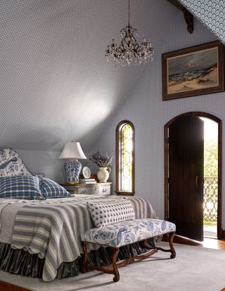 gray bedroom with wallpaper all round and gray striped throw blue and white chinoiserie print upholstered bedhead and ottoman and door open to balcony