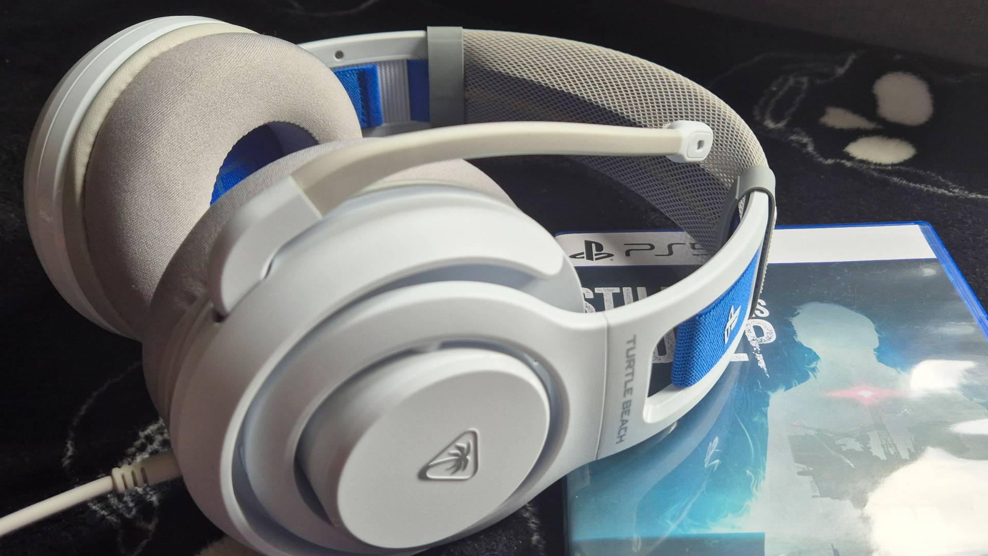 Photo of a white headset sitting on top of a PS5 game box, with a black blanket underneath them both.