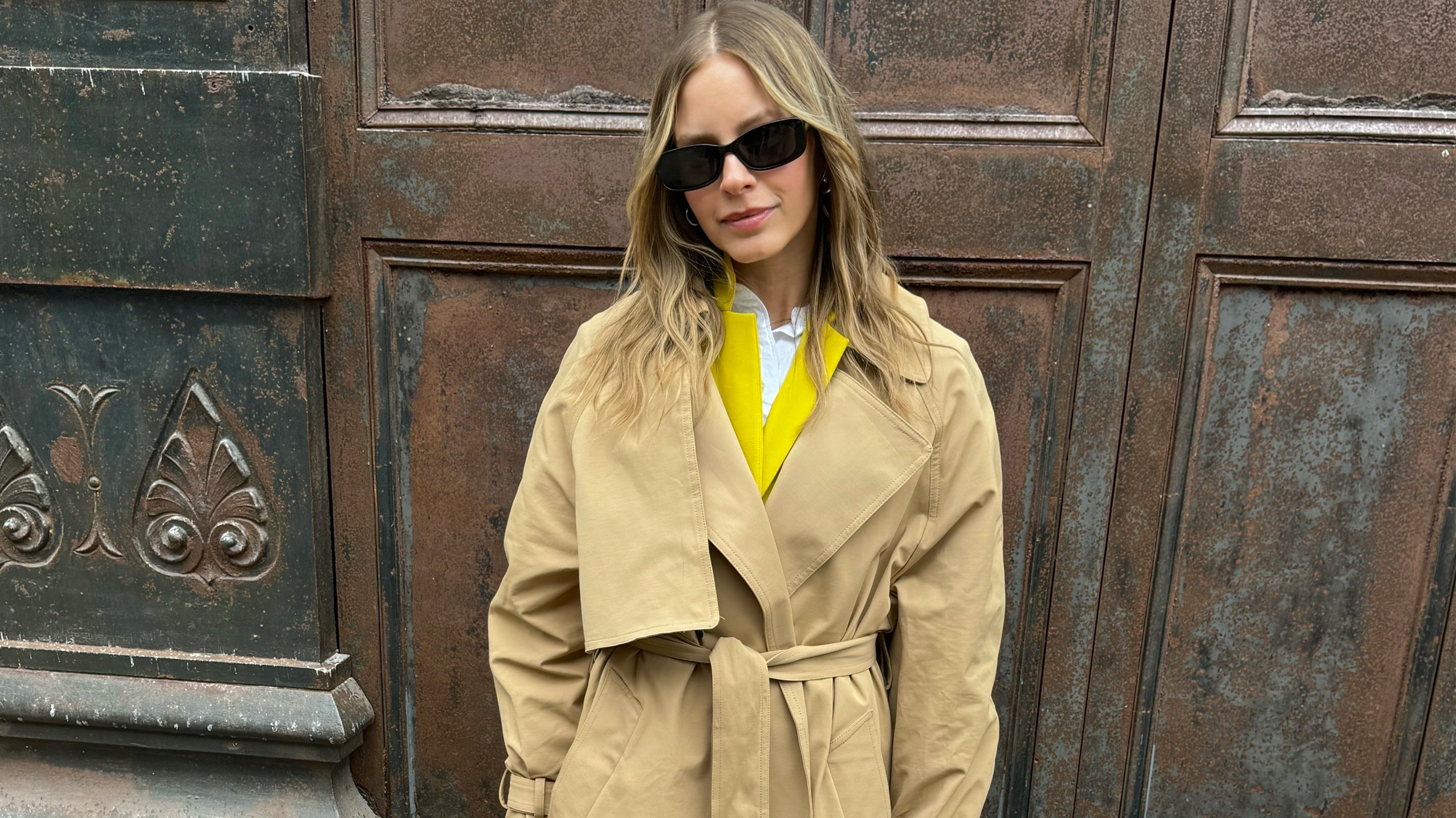 Nikki wears a trench coat with a yellow blazer.