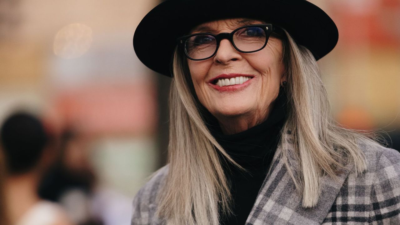 Diane Keaton wearing a hat, glasses, check blazer with a medium length hair style