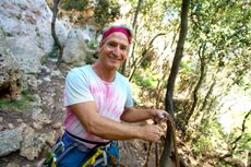 A fit, middle-aged man smiles as he pauses before technical rock climbing.