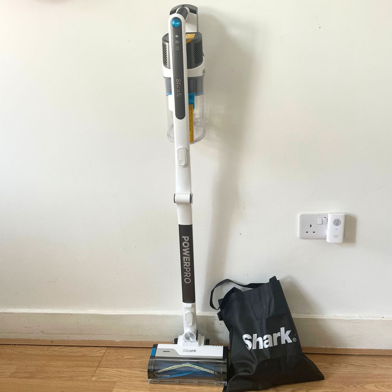 Shark PowerPro Pet Cordless Stick Vacuum leaning up against a white wall, with the accessory bag next to it