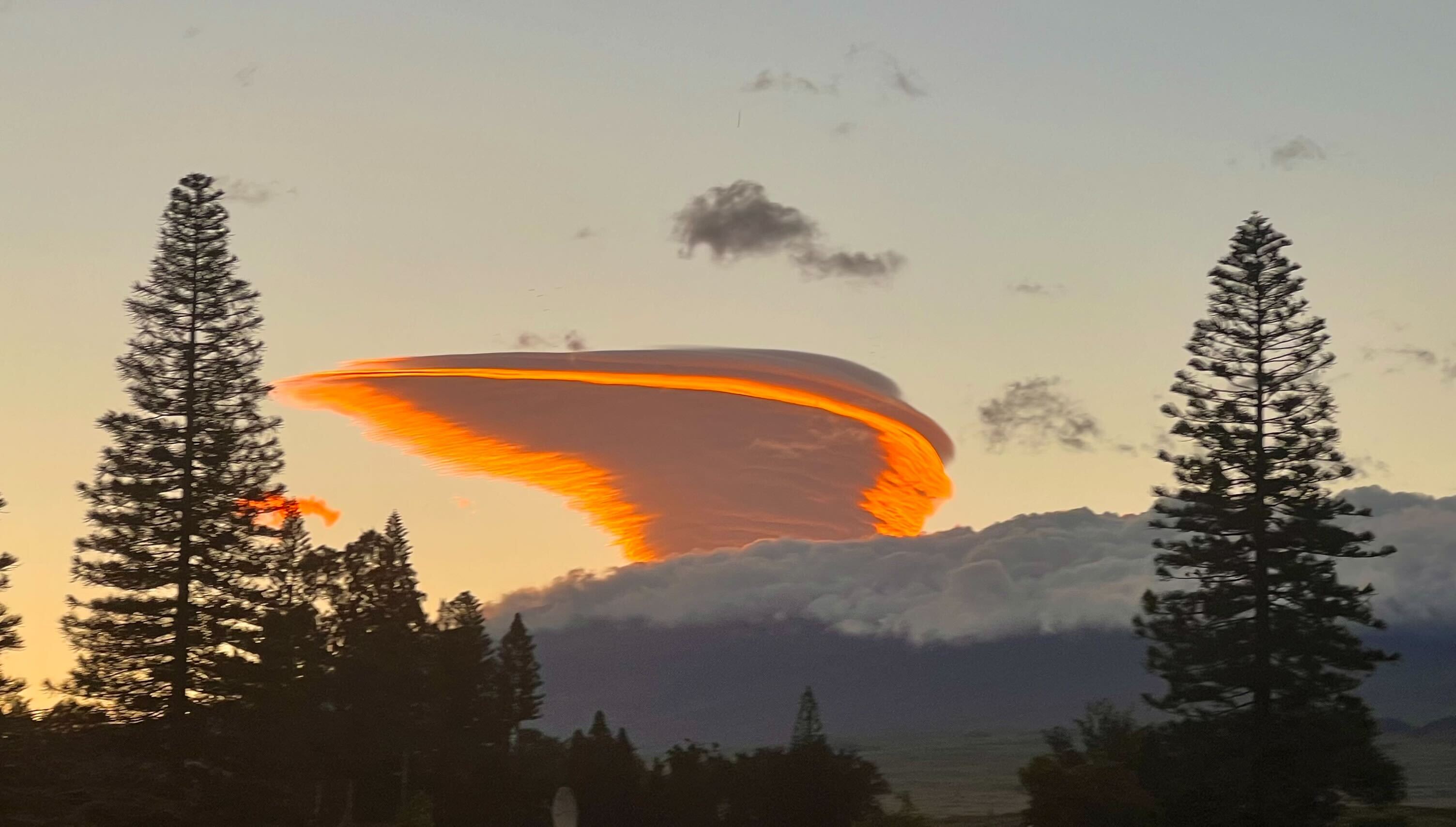 a spiral-shaped cloud is lit in bright red and gold at sunset above a mountain