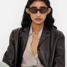 A model wearing a translucent shirt, leather jacket, and sunglasses from SSENSE. 