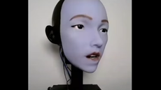 Screenshot of a robots face with lips parted,.