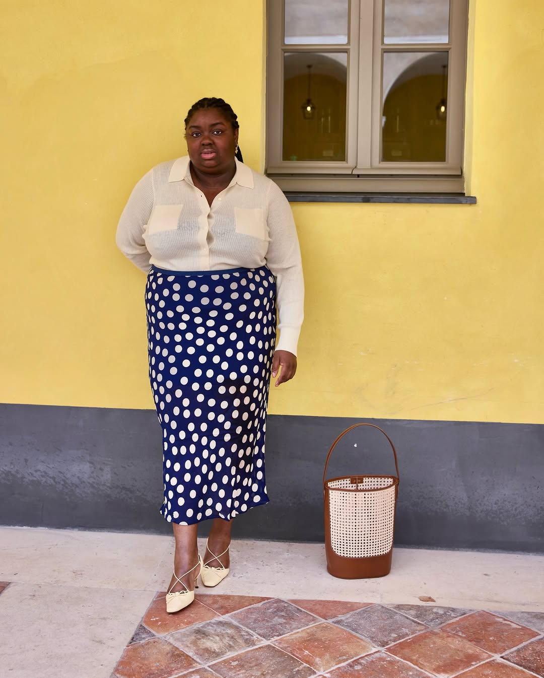 @abimarvel wears a navy polka dot satin skirt, sheer cream cardigan and strappy mules