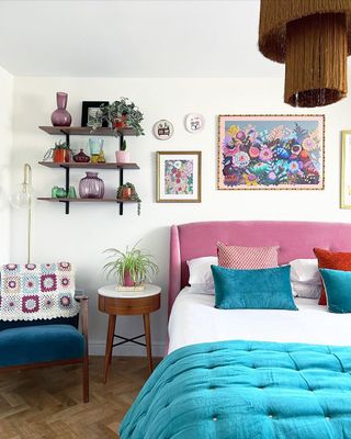 A bedroom with a pink and blue bed, wall art, shelves, and an accent chair