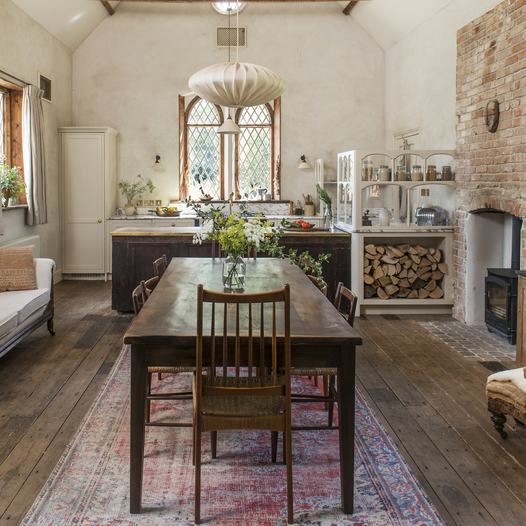 farmhouse dining table and chair in kitchen of converted school hall and cottages, with leaded arched windows and exposed brick around fireplace